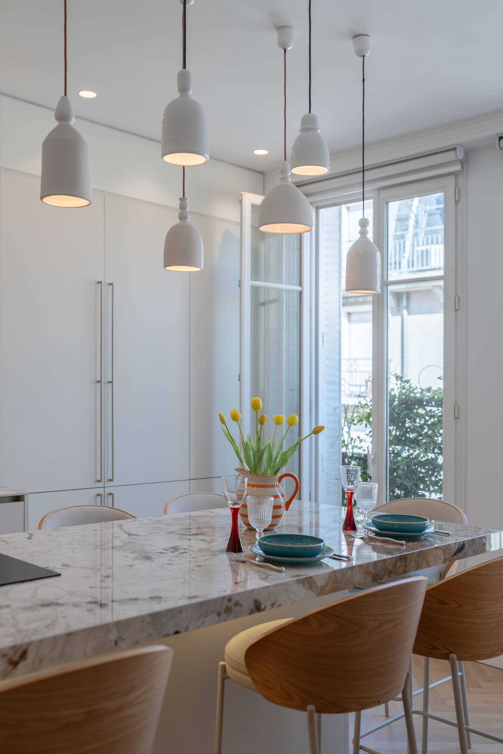 Suspensions alignées au-dessus du plan repas, devant la porte-fenêtre ouvrant sur le balcon