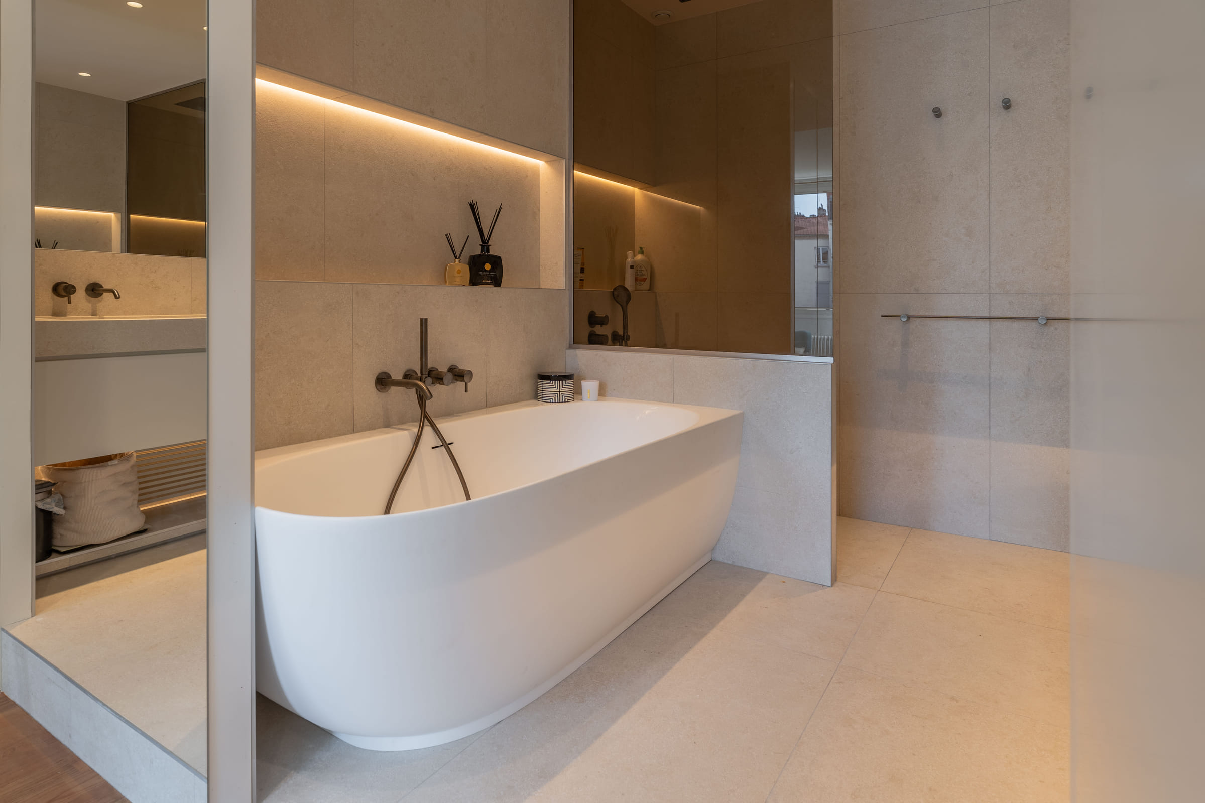 Baignoire îlot en solid surface face à la douche à l’italienne fermée par une paroi en verre fumé