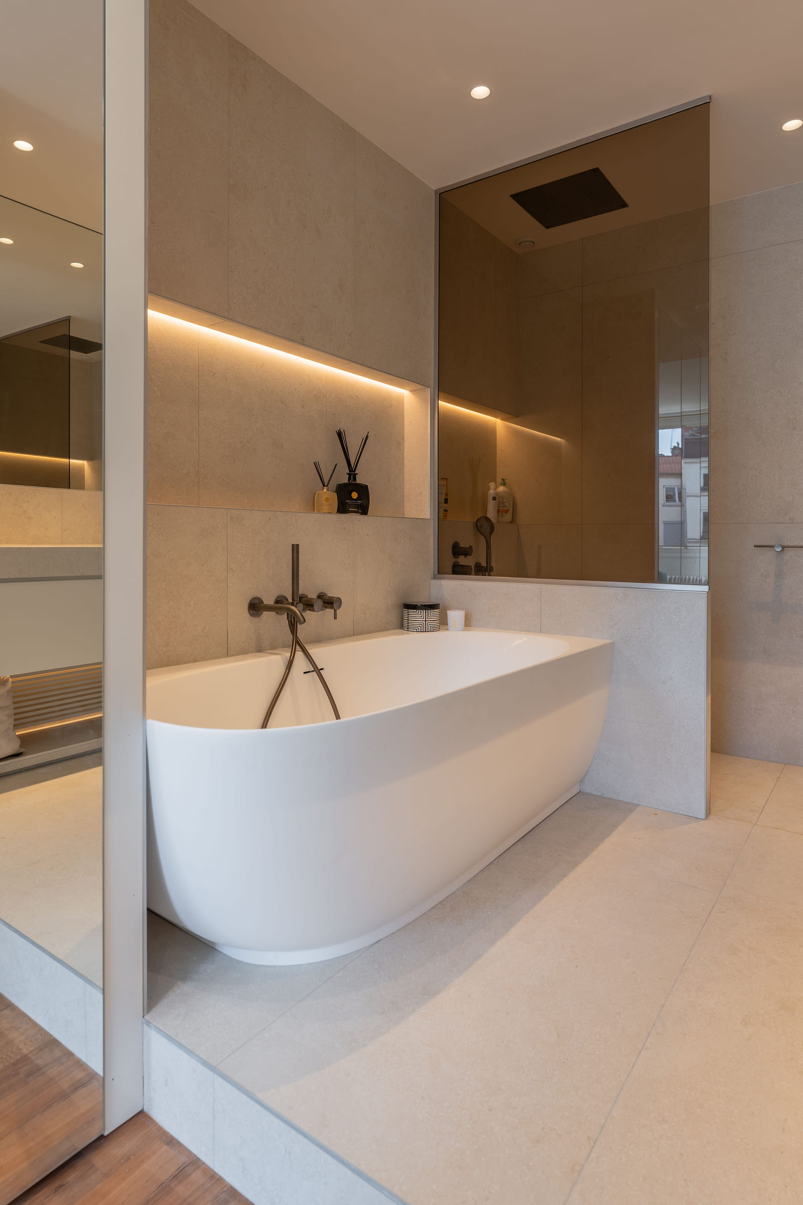 Baignoire îlot en solid surface aux lignes pleines, adossée au mur de pierre beige et à sa niche rétroéclairée