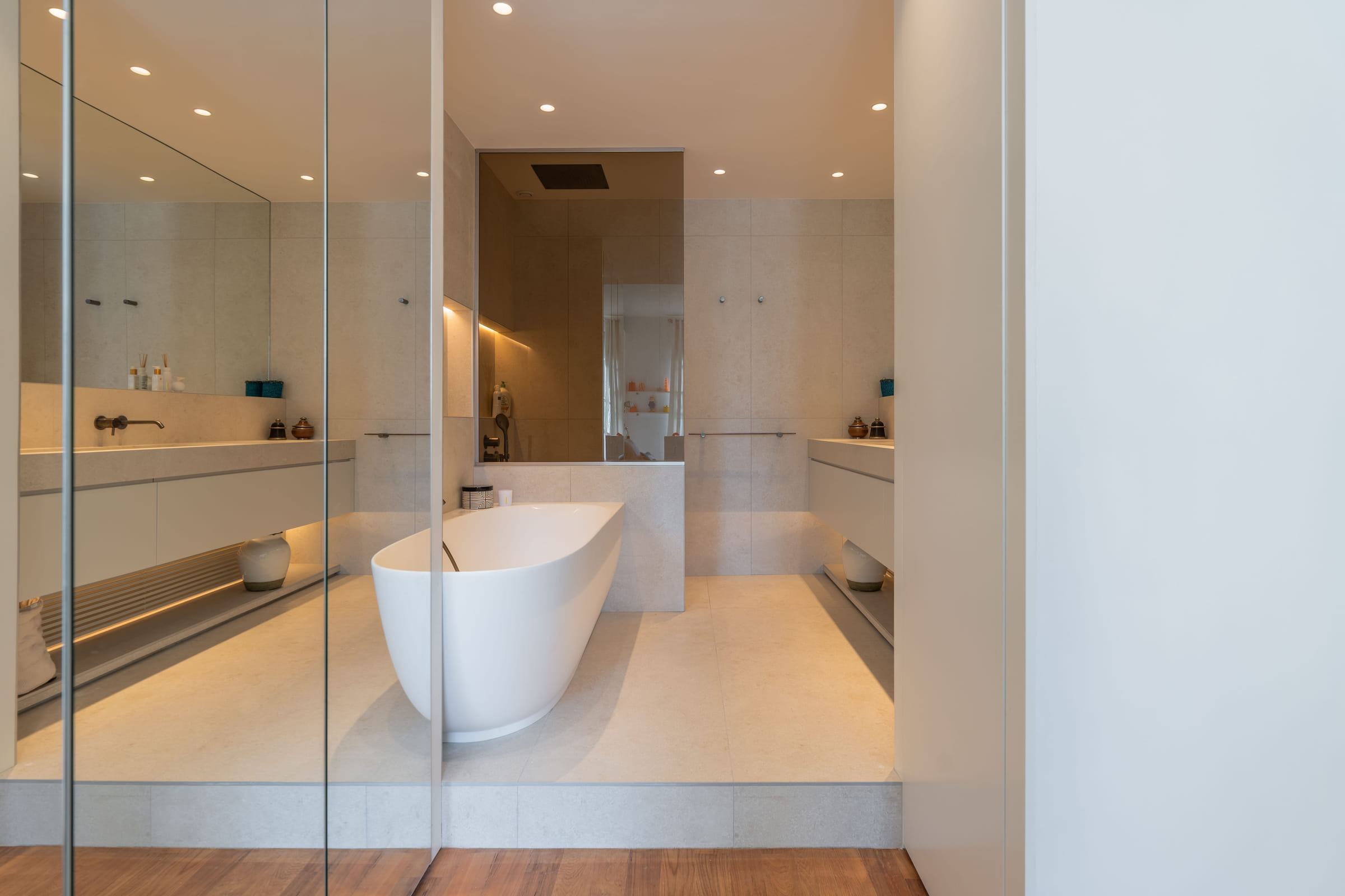 Salle de bains vue depuis la chambre, encadrée par le dressing à façades miroir, baignoire îlot au centre