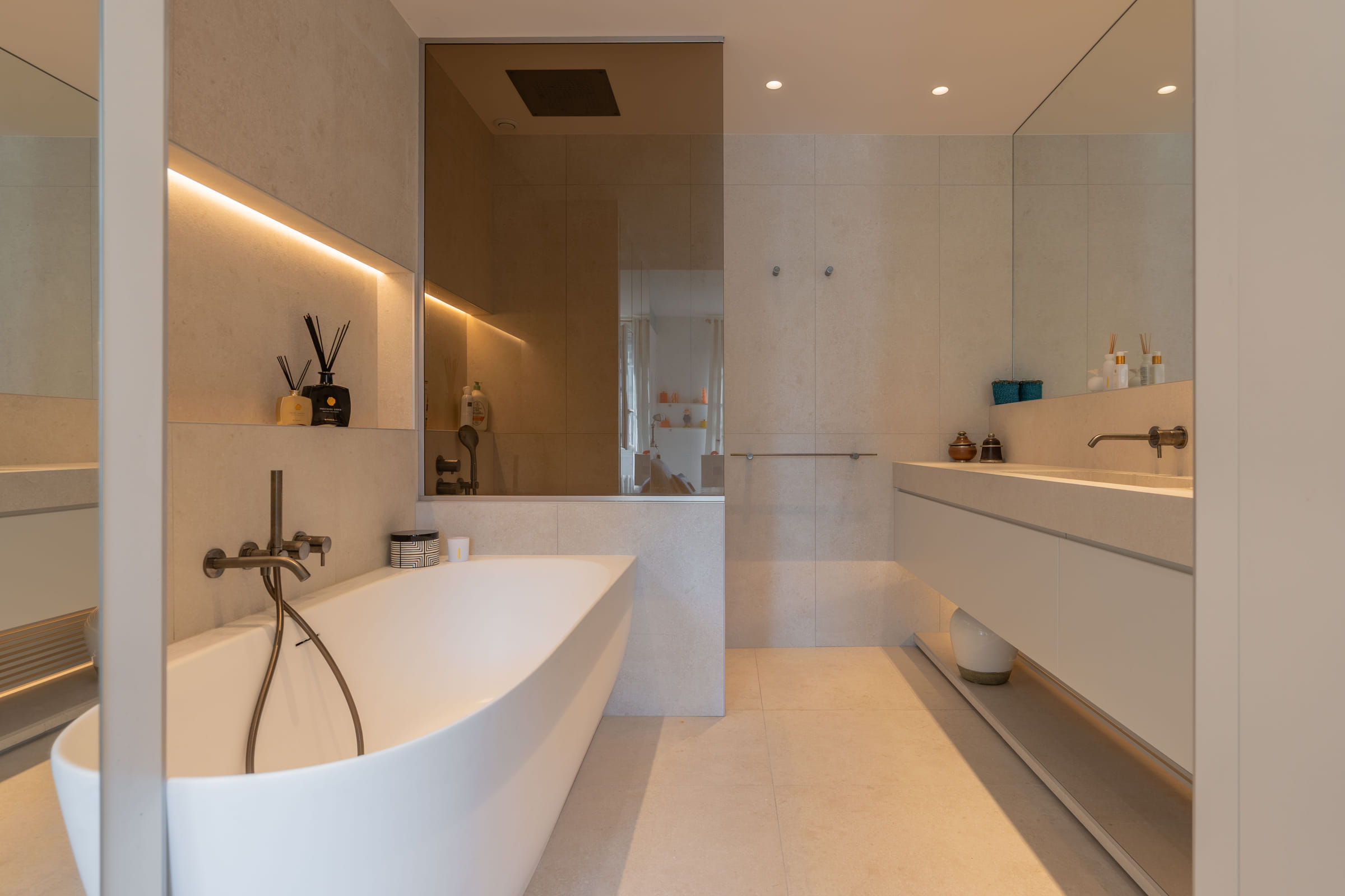 Vue d’ensemble de la salle de bains : baignoire îlot, douche à l’italienne et meuble double vasque en pierre beige